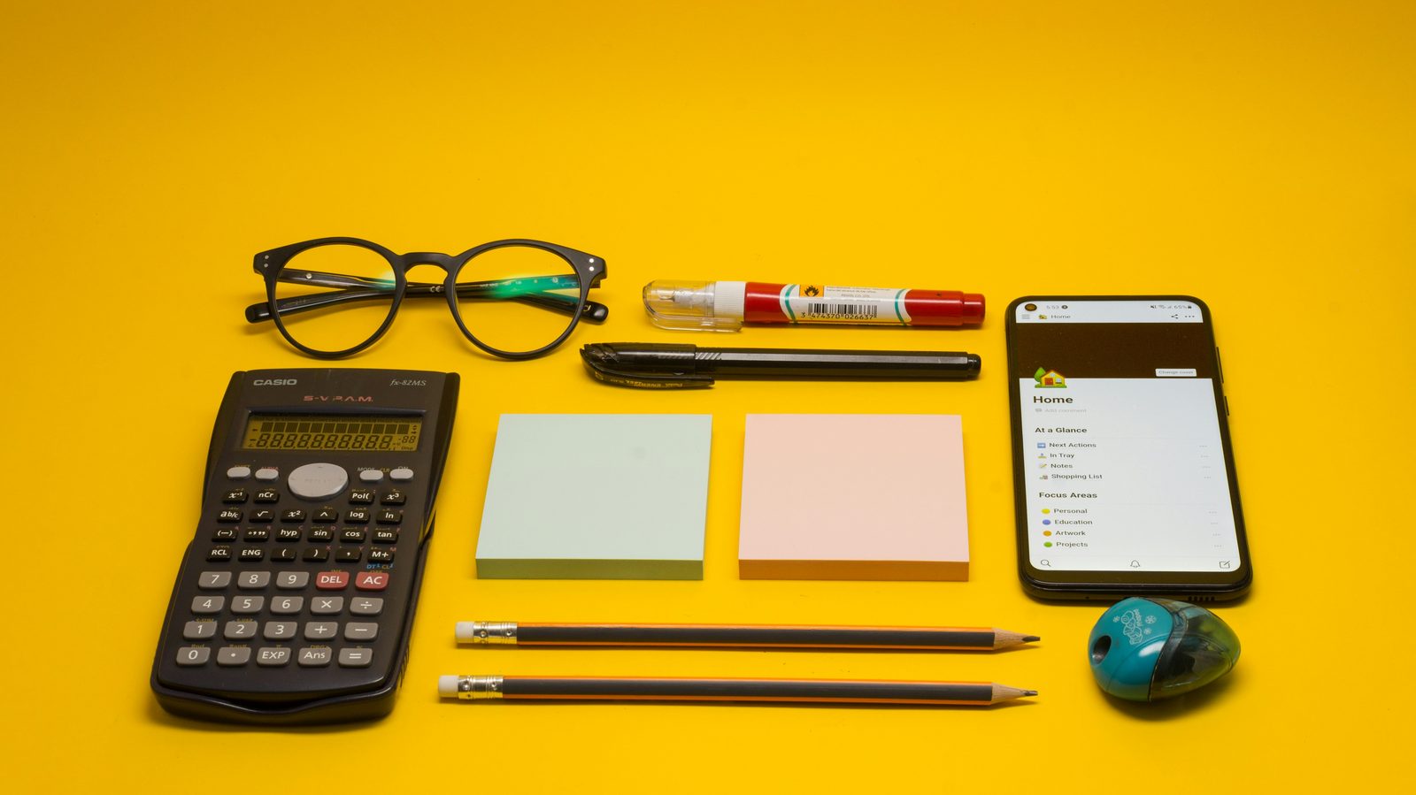 A calculator, glasses, and notebooks laid out on a desk